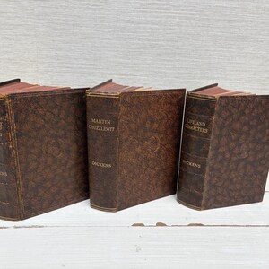 May include: Three antique books with brown leather covers are displayed. The titles include "Child's History of England," "Martin Chuzzlewit," and "Life and Characters," all by Dickens. The books have gold lettering and aged pages.