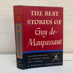 May include: A red hardback book titled "The Best Stories of Guy de Maupassant" with gold lettering. The book is part of the Modern Library series and is edited by Saxe Commins.