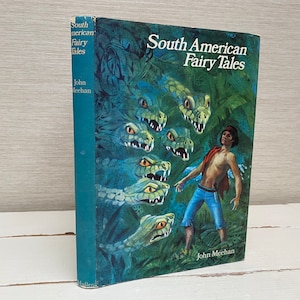 以下が含まれることがあります： 「南米の妖精物語」というタイトルの青い本の表紙。ジャングルの背景に、蛇に囲まれた少年が描かれている。著者はジョン・ミーハン。