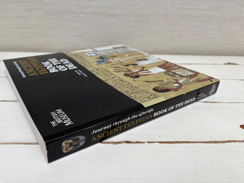 May include: A hardcover book titled "ANCIENT EGYPTIAN BOOK OF THE DEAD" from The British Museum. The book has a black spine and a cover featuring ancient Egyptian artwork. The book's title and author are visible.
