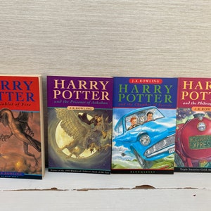 Może przedstawiać: Cztery książki w twardej oprawie w rzędzie, wszystkie należące do serii o Harrym Potterze. Książki są ułożone od lewej do prawej: Harry Potter i Czara Ognia, Harry Potter i Więzień Azkabanu, Harry Potter i Komnata Tajemnic, oraz Harry Potter i Kamień Filozoficzny.