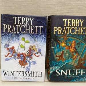 May include: Two paperback books by Terry Pratchett, "Wintersmith" and "Snuff", both featuring fantasy illustrations on the covers.