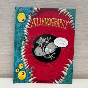 May include: A hardcover book titled "Alienography or How to Stop an Alien Invasion" with a cartoon alien illustration. The cover features a red background with a cartoon alien inside a black circle, surrounded by teeth and a blue monster.
