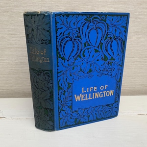 Könnte beinhalten: Ein blaues Buch mit einem goldenen Titel, der "Life of Wellington" lautet, und einem dekorativen Blumendesign auf dem Einband.