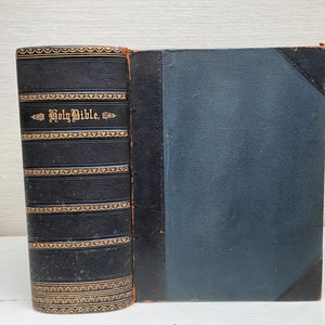 May include: A black leather-bound Holy Bible with gold lettering and decorative accents. The book is closed and lying flat on a white surface.
