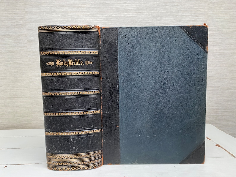 May include: A black leather-bound Holy Bible with gold lettering and decorative accents. The book is closed and lying flat on a white surface.