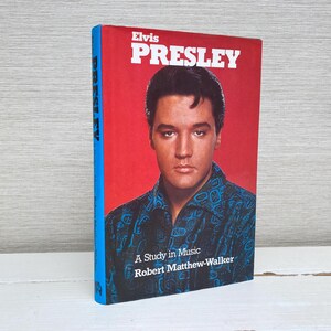 May include: A book titled "Elvis Presley" with a red cover and a portrait of Elvis Presley. The book's spine is blue. The text "A Study in Music" and the author's name, Robert Matthew-Walker, are also visible.