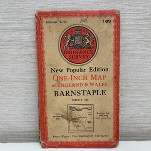 May include: A vintage Ordnance Survey one-inch map of Barnstaple, England, from the New Popular Edition. The map has a red border and a circular emblem with a coat of arms. Sheet 163, first published in 1946.