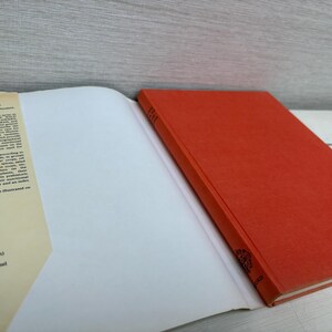 May include: An open book with a red cover and white pages. The left page has text listing plants such as coffee, vanilla, and tomato. The book is on a white surface.