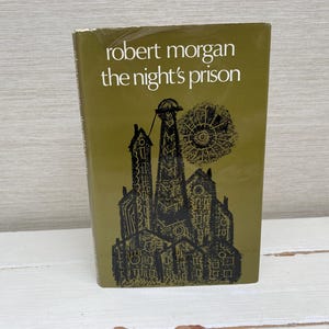 Könnte beinhalten: Ein Vintage-Buch mit dem Titel "The Night's Prison" von Robert Morgan. Das Cover ist olivgrün mit schwarzen Illustrationen von Gebäuden und einem sonnenartigen Design. Titel und Autorenname sind weiß.
