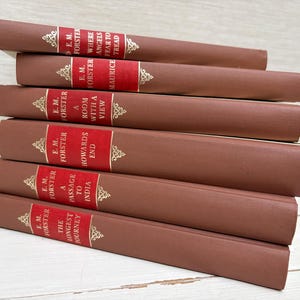 Könnte beinhalten: Ein Stapel von sechs Vintage-Büchern von E.M. Forster. Die Bücher haben braune Einbände und rote Buchrücken. Die Buchrücken zeigen den Namen des Autors und die Buchtitel in goldener Schrift. Titel sind "Howards End" und "A Passage to India".