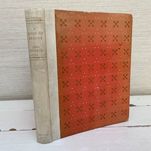 Puede incluir: Un libro antiguo de tapa dura titulado "A Book of Beauty" de John  Hampfield. La cubierta del libro presenta un diseño estampado en rojo y marrón.