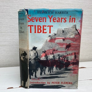 May include: A vintage hardcover book titled "Seven Years in Tibet" by Heinrich Harrer. The cover features a colorful illustration of a mountain range with a fortress on top and a group of people riding horses.