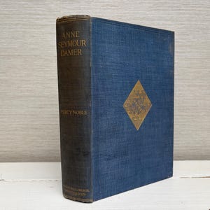 Pode incluir: Livro antigo de capa dura intitulado "Anne Seymour Damer" de Percy Noble. O livro tem uma lombada azul escura com letras douradas e uma capa azul com um emblema dourado em forma de diamante. O livro está em bom estado.