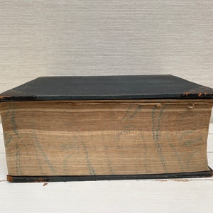 May include: A large, black, hardcover book with a brown spine and a decorative pattern on the cover. The book is closed and sitting on a white surface.