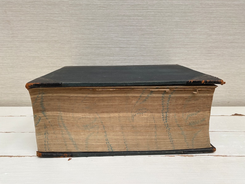 May include: A large, black, hardcover book with a brown spine and a decorative pattern on the cover. The book is closed and sitting on a white surface.