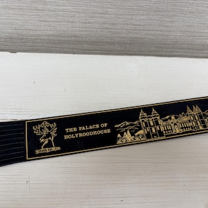 May include: A black bookmark with gold text and a fringed edge. The bookmark features an illustration of a building and the text "THE PALACE OF HOLYROODHOUSE". A deer emblem is also present.