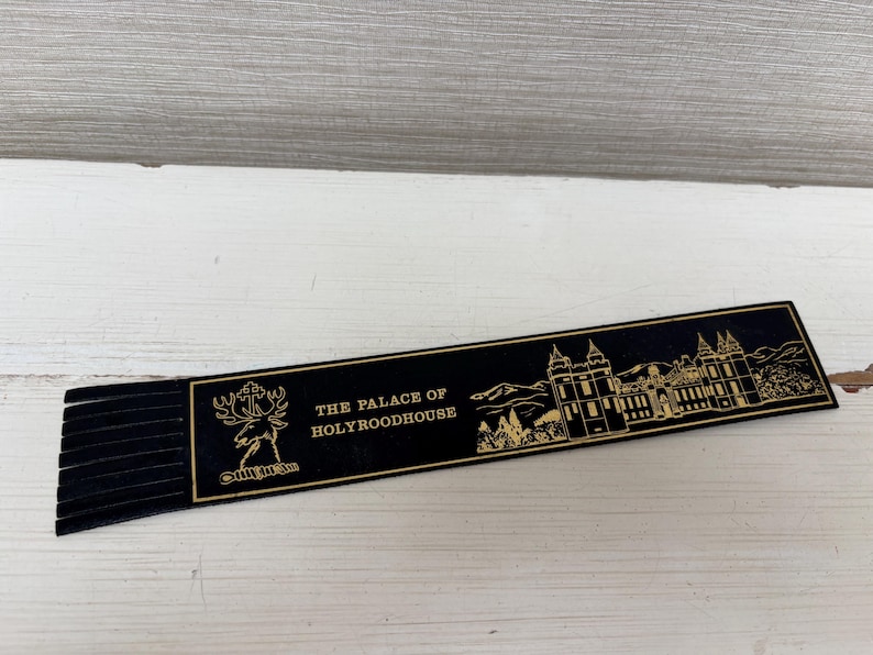 May include: A black bookmark with gold text and a fringed edge. The bookmark features an illustration of a building and the text "THE PALACE OF HOLYROODHOUSE". A deer emblem is also present.