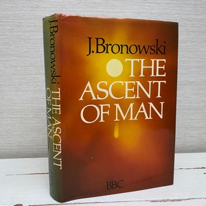 Könnte beinhalten: Ein braunes Buch mit dem Titel "The Ascent of Man" von J. Bronowski. Der Buchumschlag zeigt einen gelben und orangen Farbverlauf mit einem weißen Kreis in der Mitte. Das BBC-Logo befindet sich am unteren Rand des Umschlags.