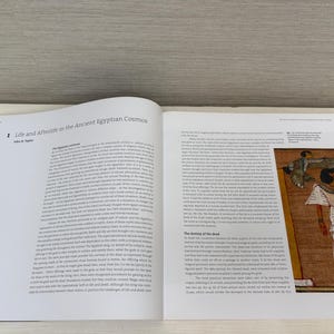 May include: An open book with the title "Life and Afterlife in the Ancient Egyptian Cosmos" is displayed. The right page features an illustration of an Egyptian figure in a white robe, with hieroglyphs and text.