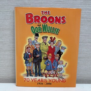 Pode incluir: Capa de livro laranja com o título "THE BROONS and OOR WULLIE" em letras vermelhas e verdes. Ilustração em grupo de personagens de desenhos animados. Texto "70 YEARS YOUNG 1936-2006".