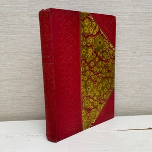 Op de afbeelding: Een rood hardback boek met een gouden marmerachtige rug. Het boek heeft een decoratief reliëfpatroon op de omslag.