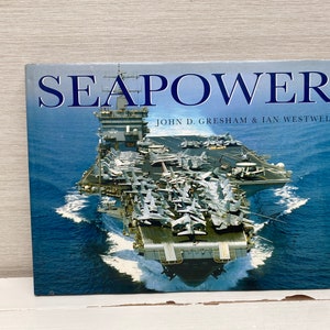 May include: A book titled "Seapower" by John D. Gresham & Ian Westwell, featuring a photograph of a large aircraft carrier with fighter jets on the deck, sailing on a blue ocean.