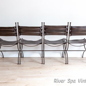 May include: Four brown leather-backed chairs with metal frames. The chairs are arranged in a row, facing forward. The chairs have a simple, rustic design.
