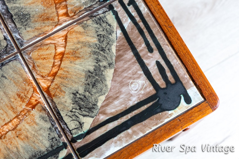May include: A vintage coffee table with a tiled top. The tiles are brown, white, and black with abstract designs. The table has a wooden frame.