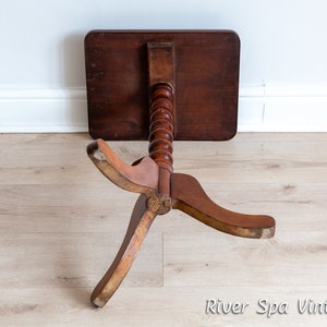 May include: A wooden side table with a turned pedestal base and three legs. The table top is dark brown and the base is a lighter brown.