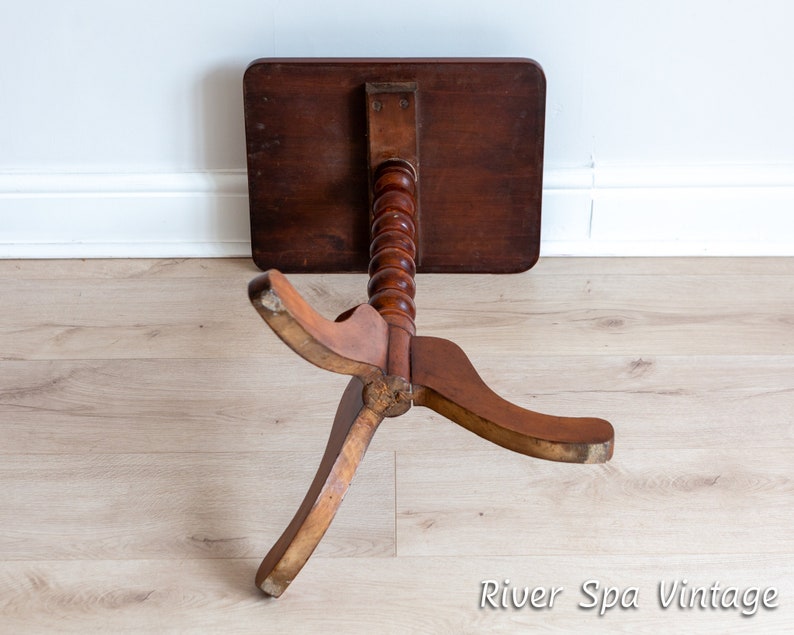 May include: A wooden side table with a turned pedestal base and three legs. The table top is dark brown and the base is a lighter brown.