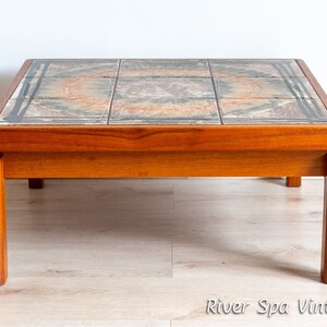 May include: A mid-century modern coffee table with a tiled top featuring a geometric pattern in shades of brown, beige, and blue. The table has a teak wood frame and four legs.