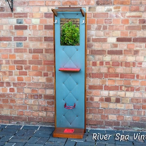 May include: A vintage wooden coat rack with a blue upholstered back panel, a small mirror, and a shelf. The rack has a red shelf and a red metal hook.