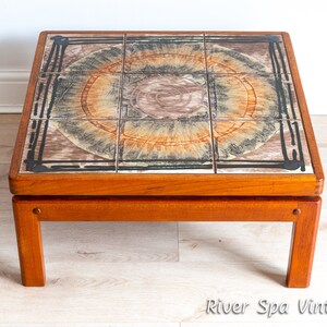 May include: A mid-century modern coffee table with a tiled top featuring a geometric pattern in shades of brown, orange, and black. The table has a solid wood frame and legs.