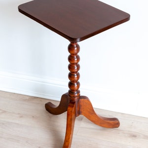 May include: A dark brown wooden side table with a square top and a turned, beaded leg. The table has three curved legs.