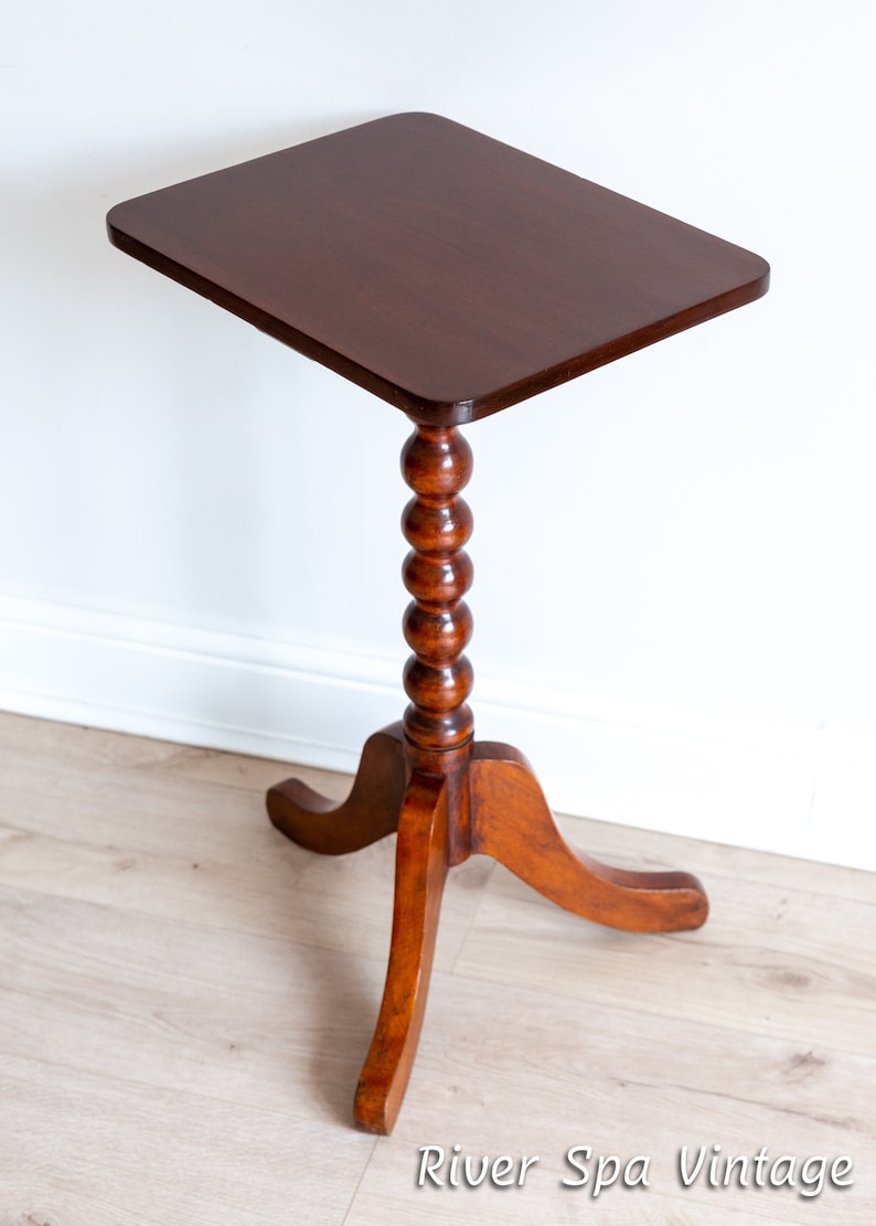 May include: A dark brown wooden side table with a square top and a turned, beaded leg. The table has three curved legs.