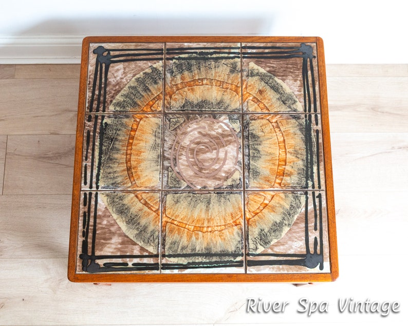 May include: A square, wooden coffee table with a tiled top. The tiles are brown, black, and orange with a swirling pattern. The table is in good condition and has a vintage look.