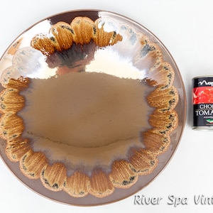 May include: A large, brown ceramic serving dish with a scalloped edge and a brown and gold glaze. The dish has a reflective surface and a unique design.