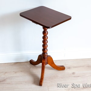 May include: A dark brown wooden side table with a square top and a turned, beaded leg. The table has a three-legged base with curved legs.