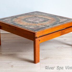 May include: A square, mid-century modern coffee table with a tiled top. The tiles are a mix of brown, orange, and green with a geometric pattern. The table has a solid wood frame and legs.
