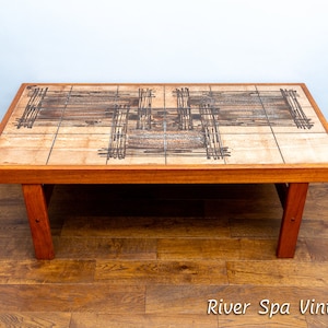 May include: A mid-century modern coffee table with a tiled top featuring a geometric pattern in shades of brown and beige. The table has a solid wood frame and legs.