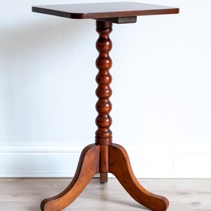 May include: A dark brown wooden side table with a square top and a turned, fluted pedestal base. The base has three curved legs.