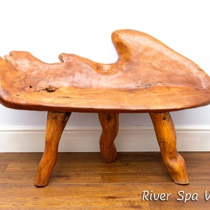 Puede incluir: Un banco de madera rústico con una forma orgánica única. El banco está hecho de madera natural con un color marrón cálido y tiene cuatro patas que están talladas en la misma madera. El banco es perfecto para agregar un toque de naturaleza a cualquier espacio.