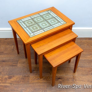 Könnte beinhalten: Ein Satz von drei verschachtelten Tischen aus Holz mit einer gekachelten Tischplatte. Der oberste Tisch hat ein geometrisches Muster in Blau- und Grüntönen. Die Tische sind in absteigender Reihenfolge angeordnet.