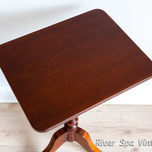 May include: A dark brown wooden side table with a square top and a turned pedestal base. The table is on a light wood floor.
