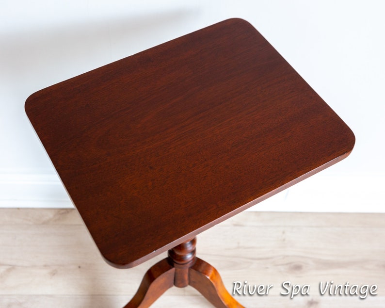 May include: A dark brown wooden side table with a square top and a turned pedestal base. The table is on a light wood floor.