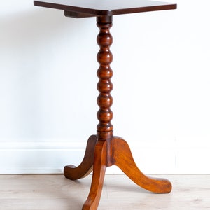 May include: A dark brown wooden side table with a square top and a turned, fluted leg. The table has three legs that splay out from the base.
