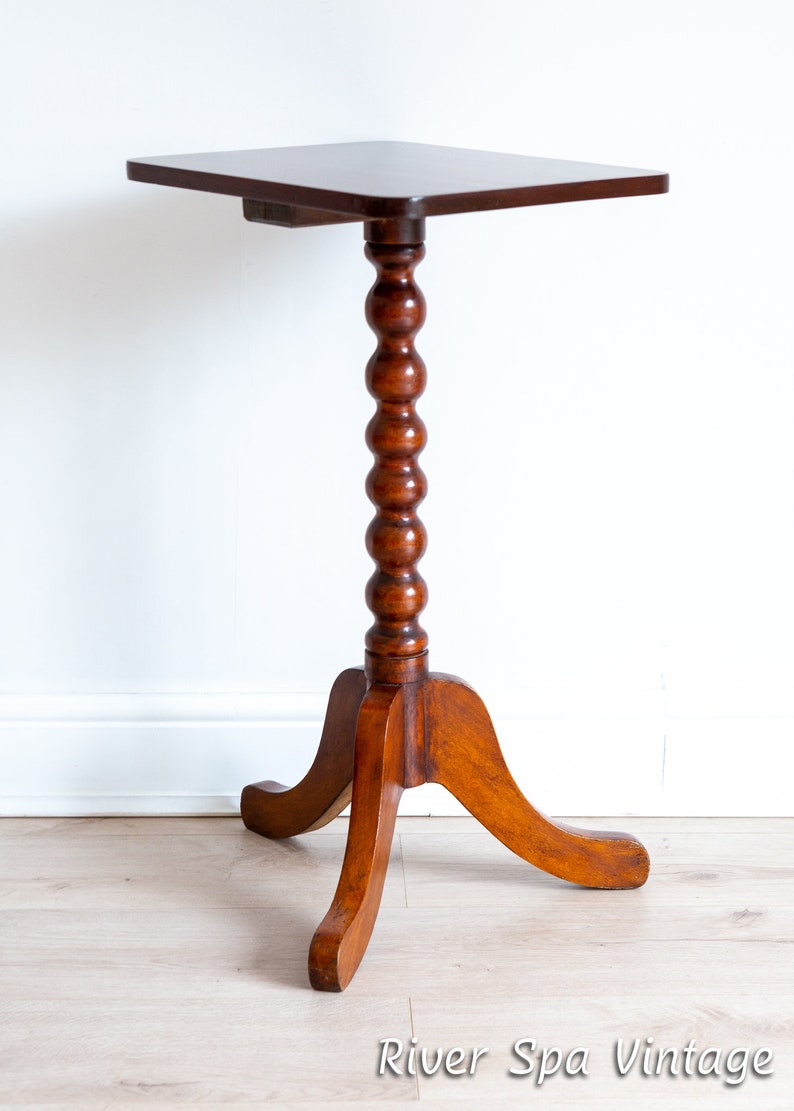 May include: A dark brown wooden side table with a square top and a turned, fluted leg. The table has three legs that splay out from the base.