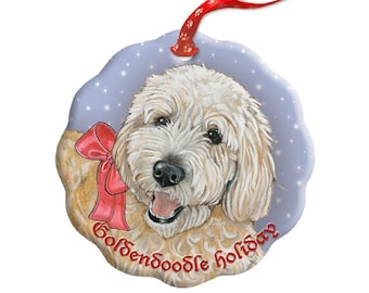 May include: A round ceramic Christmas ornament featuring a golden doodle dog with a red bow. The ornament has a blue background with white snowflakes and the text "Golden doodle holidays".