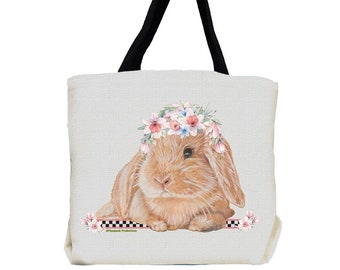May include: A white canvas tote bag with black handles features a brown bunny wearing a pink and white flower crown. The bunny is lying down with its paws crossed. The bag has a black and white checkered stripe and a pink stripe at the bottom.